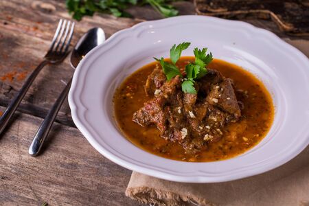 Beef with spicy sauce and parsley a white plate on rustic wooden table top viewの写真素材