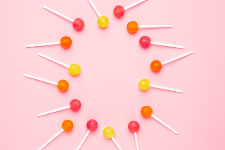 Pink, orange and yellow sweet candy lolipop on a pastel pink background top view.