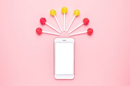 Mobile phone with pink and yellow candy on a pastel pink background top viewの写真素材