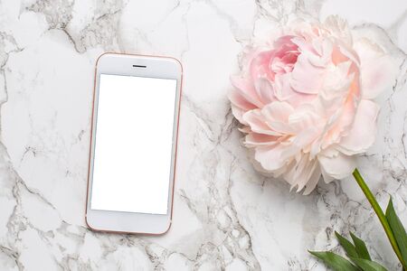 Mobile phone with a white and pink piony flowers on a marble background flat layの写真素材