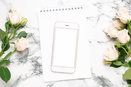 Mobile phone with a white and pink notebook and roses flowers on a marble background top viewの写真素材