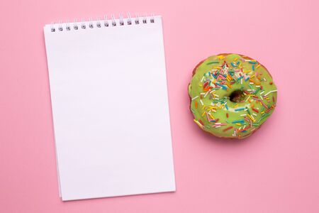 Notebook and sweet green donut with sprinkle on a pink background flat lay top viewの写真素材