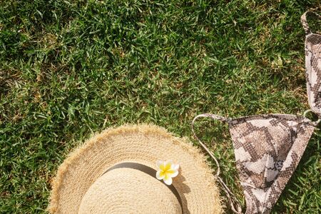 Straw hat and female swimsuit on green grass.Summer vacation concept top view.の写真素材