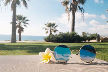 Sunglasses and flowers on a beach lounge chair side view . Tropical summer vacation concept. Happy...