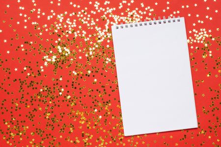 Notebook and golden stars confetti on red color paper background minimal style, christmas and new year concept top viewの写真素材