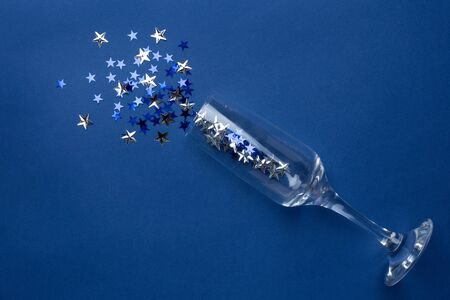 Champagne glass with silver blue stars confetti on classic blue color background minimal styleの写真素材