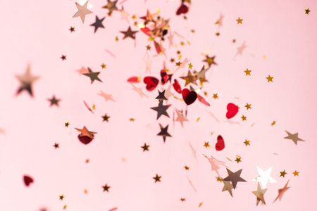Silver, red and gold star confetti on pastel pink background side view. Bright and festive holiday...