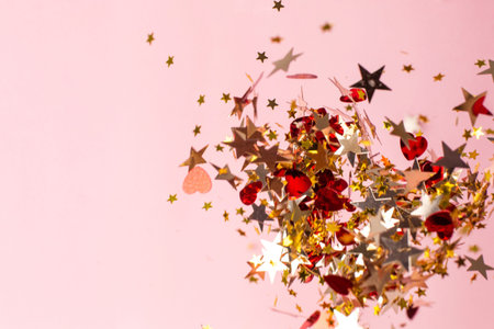 Silver, red and gold star confetti on pastel pink background. Bright and festive holiday background.