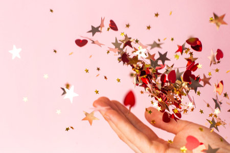 Gold star confetti in women's hand on pastel pink background side view.Bright and festive holiday background.の写真素材