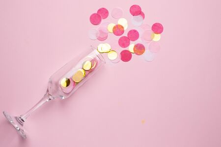 Champagne glass with golden and pink confetti on pink color paper background minimal styleの写真素材