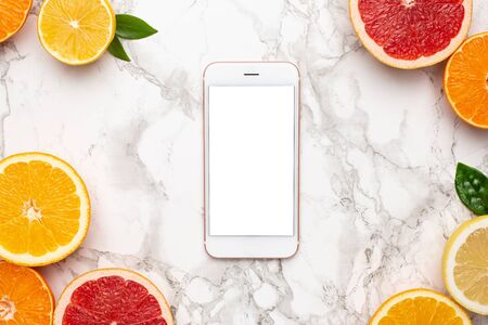 Mobile phone and citruses on marble background, fruit flatlay, summer minimal compositon with grapefruit, lemon, mandarin and orange op viewの写真素材