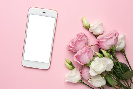 Mobile phone with pink and white roses flowers on pastel background side view.Minimalistic composition for the holidays,valentines day and womens day.の写真素材