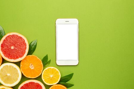 Mobile phone and citruses on an green background, technology and fruit flatlay, summer minimal compositon with grapefruit, lemon, mandarin and orange top viewの写真素材