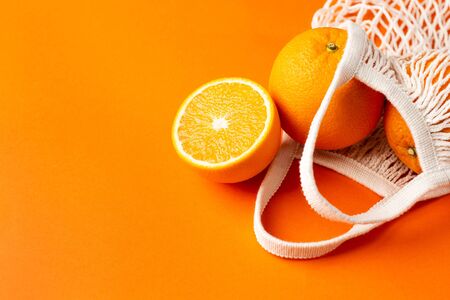 Cutting orange in cotton shopping eco friendly bag on orange background. Citrus harvest, monochrome composition with copyspace side viewの写真素材