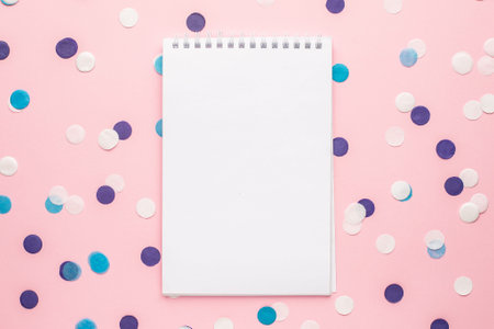 Notebook and blue, white and lilac confetti on pink color paper background minimal style top view