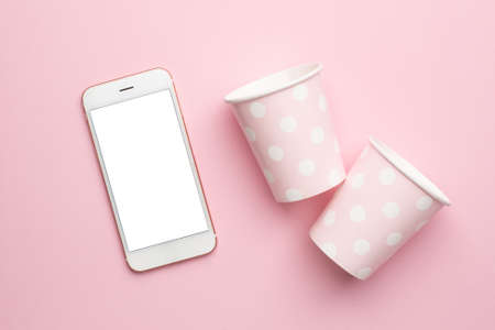 Mobile phone and polka dot disposable paper cups on pink backgroundの写真素材