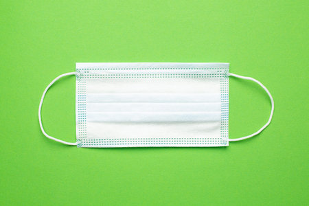 Medical mask on a green background, pandemic second wave and protection from covid infection