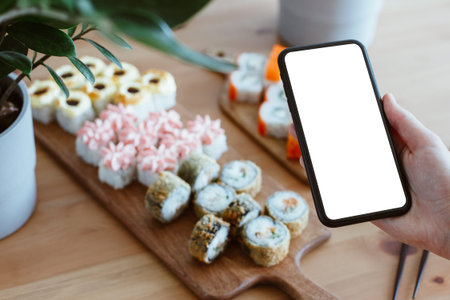 Japanese rolls and mobile phone in hand on a wooden backgroundJapanese rolls and mobile phone in...