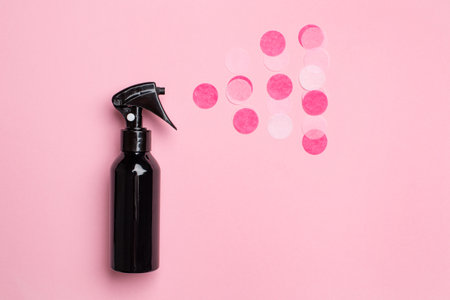 Black spray bottle with confetti on pastel pink background top viewの写真素材