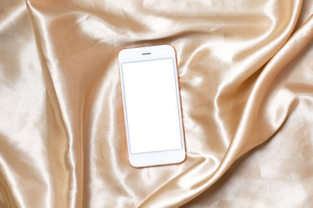 Flat lay concept of feminine light background with mobile phone on Beige silk .White screen with copy space top view.の写真素材