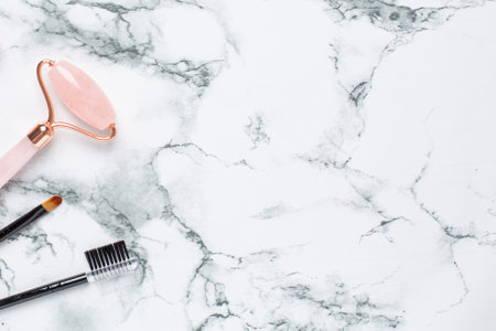 Pink Gua Sha massage tool on a marble background, close-up. Rose Quartz jade roller. Facial skin care at home, anti-aging and lifting therapy side viewの写真素材