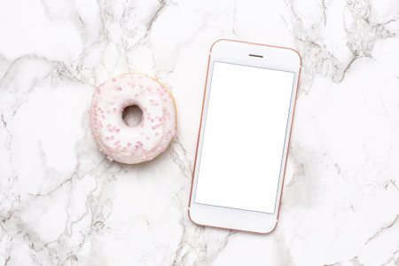 Mobile phone and sweet donut on a marble background flat lay, technology and sweet foodの写真素材