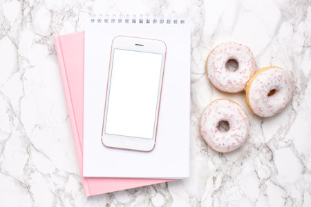 Mobile phone,pink notebook and sweet donut on a marble background flat lay, technology and sweet foodの写真素材