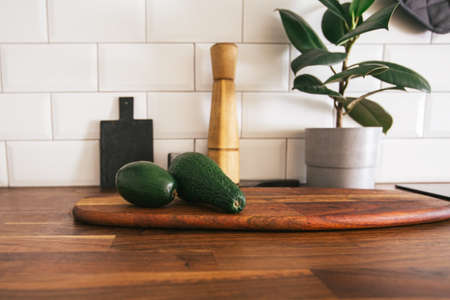 Kitchen brass utensils, chef accessories. Hanging kitchen with white tiles wall and wood tabletop.Green plant and avocado on kitchen backgroundの写真素材
