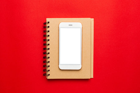 Office Workplace with Notepad , Mobile Phone with white screen on red background . Valentines Day and shopping conceptの写真素材