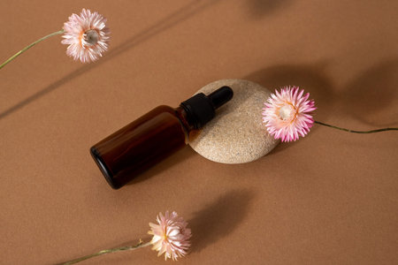 Brown glass bottle dropper with cosmetic oil with pink dry flowers on terracotta background front view, closeupの写真素材