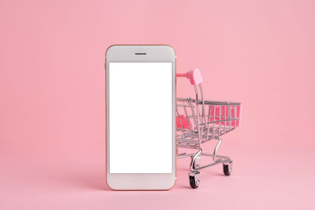 Mobile phone screen in shopping cart model on pink pastel background with copy space, delivery and online shopping. High quality photo side viewの写真素材