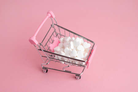 A supermarket cart filled to the brim with white candy hearts on a pink background. The concept of buying presents top viewの写真素材