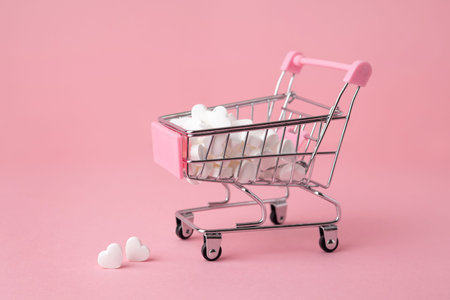 A supermarket cart filled to the brim with white candy hearts on a pink background. The concept of buying presents side viewの写真素材