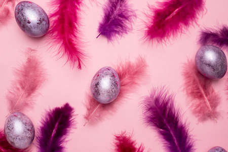 Easter holiday. Beautiful eggs lie on abstract pink and purple feathers on pastel background. Feathers all around. top viewの写真素材