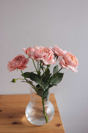 Pink rose in vase on wooden table on gray wall background verticalの写真素材