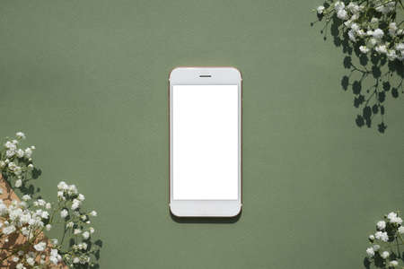 Mobile phone mock up on a pastel green background decorated with white small flowers top viewの写真素材