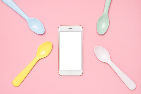 Mobile phone mock up and Kid spoons in different colors laid on sweet pink pastel background, a set of colorful spoons, pastel palette spoons and technologyの写真素材