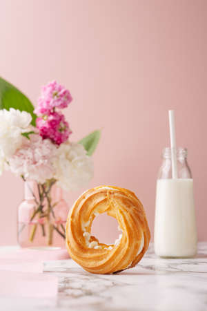 Homemade circle profiterole with custard covered sugar powder on marble table on pink background with flowers and milkの写真素材