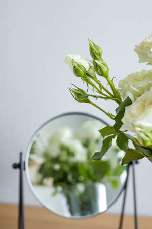 Bouquet of small delicate white cream roses in a vase with mirror on the table vertical shotの写真素材