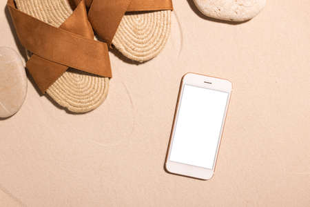 Beach background with mobile phone ,brown sandals and stone on a sandy beach in the sun. Concept: Summer vacation in a warm country.の写真素材