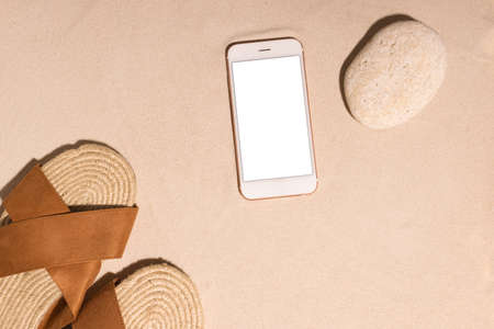 Beach background with mobile phone ,brown sandals and stone on a sandy beach in the sun. Concept: Summer vacation in a warm country.の写真素材