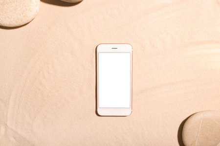 Beach background with mobile phone and stone on a sandy beach in the sun. Concept: Summer vacation in a warm country.の写真素材