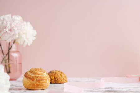 Homemade profitroles pastry filled with custard. Eclairs with cream, French dessert and flowers on marble table on pink backgroundの写真素材