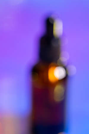 Blur oily serum in glass bottle with pipette on pink and purple background, neon light with copy space. Modern and futuristic cosmeticの写真素材