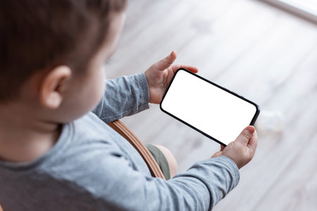 Boys toddler hands holdingphone on home background. Childs hands hold black smartphone and watching...