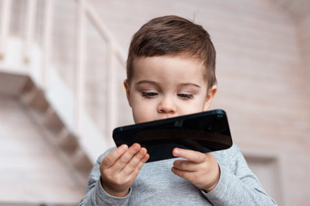 Cute little toddler boy playing with smartphone Healthy baby touching mobile phone with fingers,...