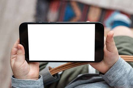 Boys toddler hands holdingphone on home background. Childs hands hold black smartphone and watching video in horizontal position. Screen blank. Close-Up.の写真素材