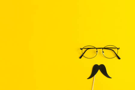Fathers Day Holiday Concept. Transparent glasses, stylish black paper photo booth props moustaches on yellow background.の写真素材