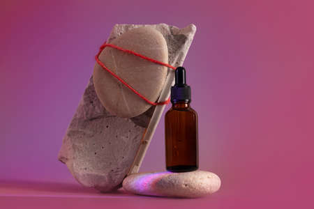 Brown glass bottle of cosmetic product or oil on stone in red light background. Futuristic Cosmetic Beauty concept , modern beautyの写真素材