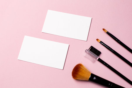 Makeup brush and white business card on pink background. A horizontal template for a makeup artists business card or flyer design, with copy spaceの写真素材